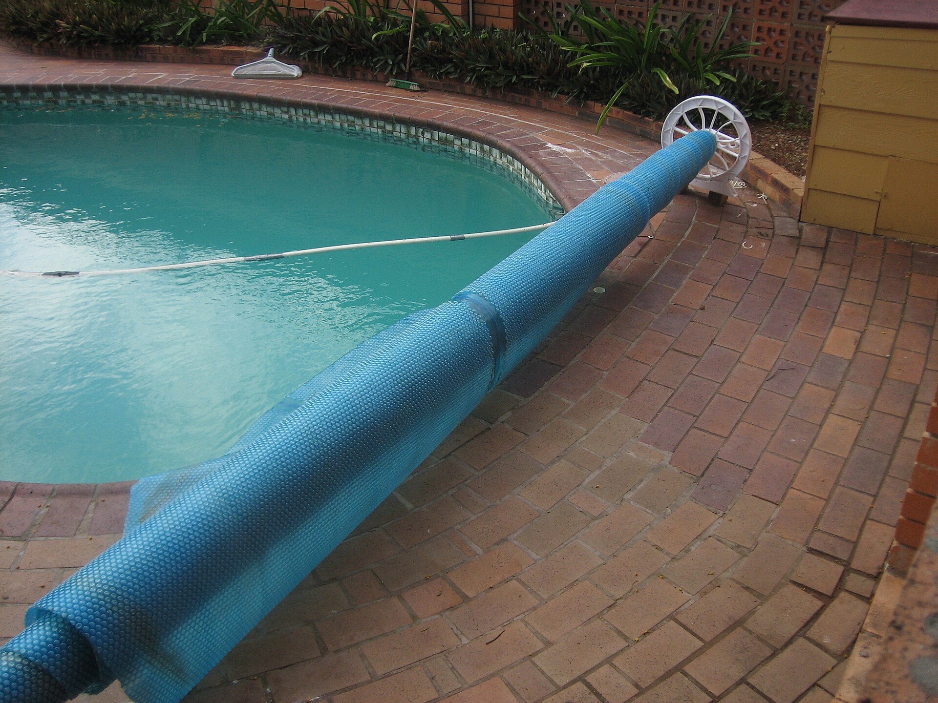 bâche de piscine enroulée sur son support, abri de jardin en arrière-plan
