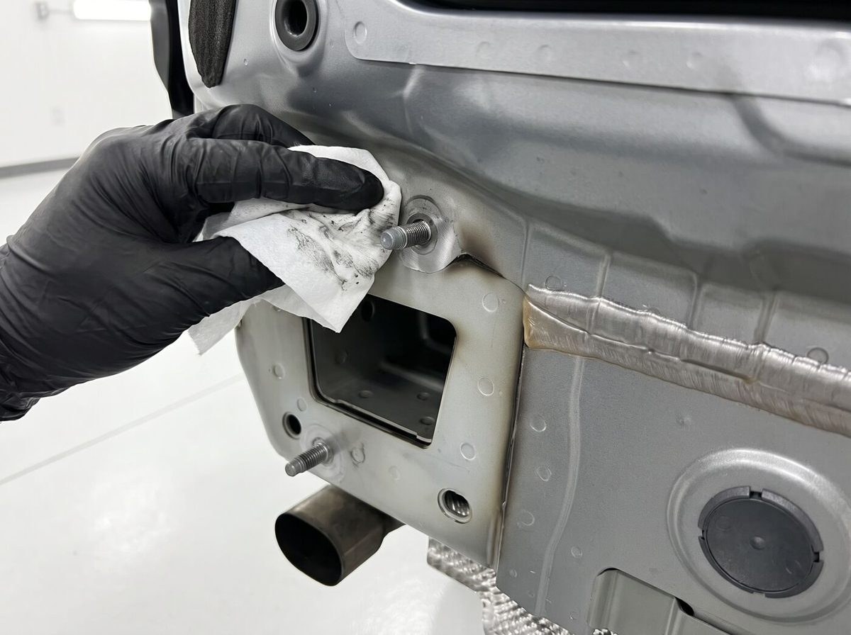 Main gantée nettoyant un point d'ancrage fileté sur le châssis d'une voiture